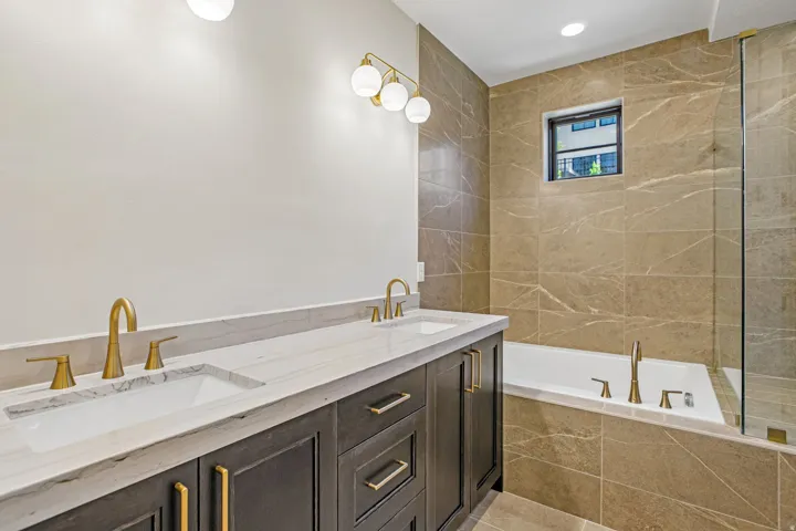 Bathroom featuring a double vanity with white countertops, dark wood cabinetry, and gold-finish hardware and fixtures