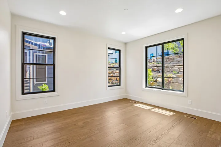 Bright room featuring three black-framed windows, recessed lighting, white walls, and wood-finish flooring
