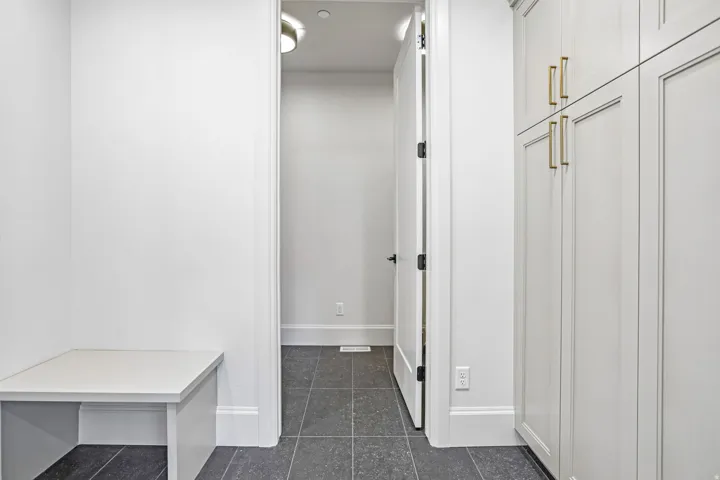 Mudroom featuring extensive built-in cabinetry with gold-tone hardware, built-in bench seating, dark tile flooring, and a white interior door with black hardware