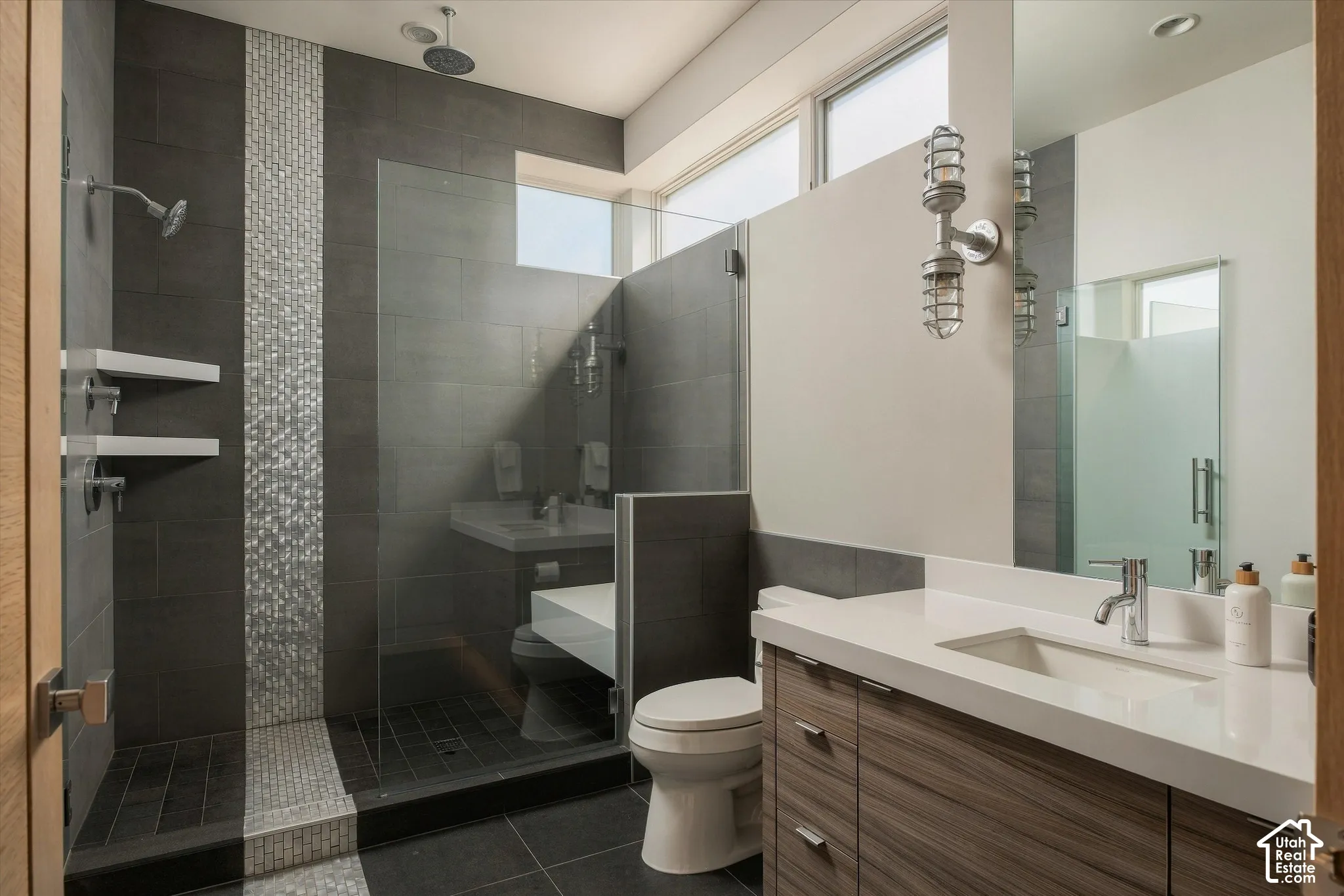 Spacious bathroom featuring a glass-enclosed shower with contrasting tile mosaic, dual shower heads, and built-in shelving