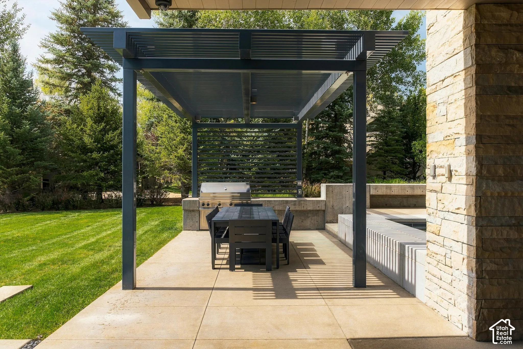 Outdoor living space featuring a modern pergola, concrete patio, built-in BBQ, and stone-clad architectural elements