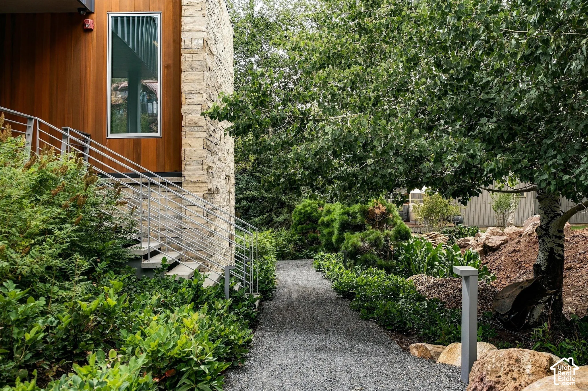 Exterior with stone cladding and wood paneling, featuring a contemporary window, metal railings, and a gravel pathway