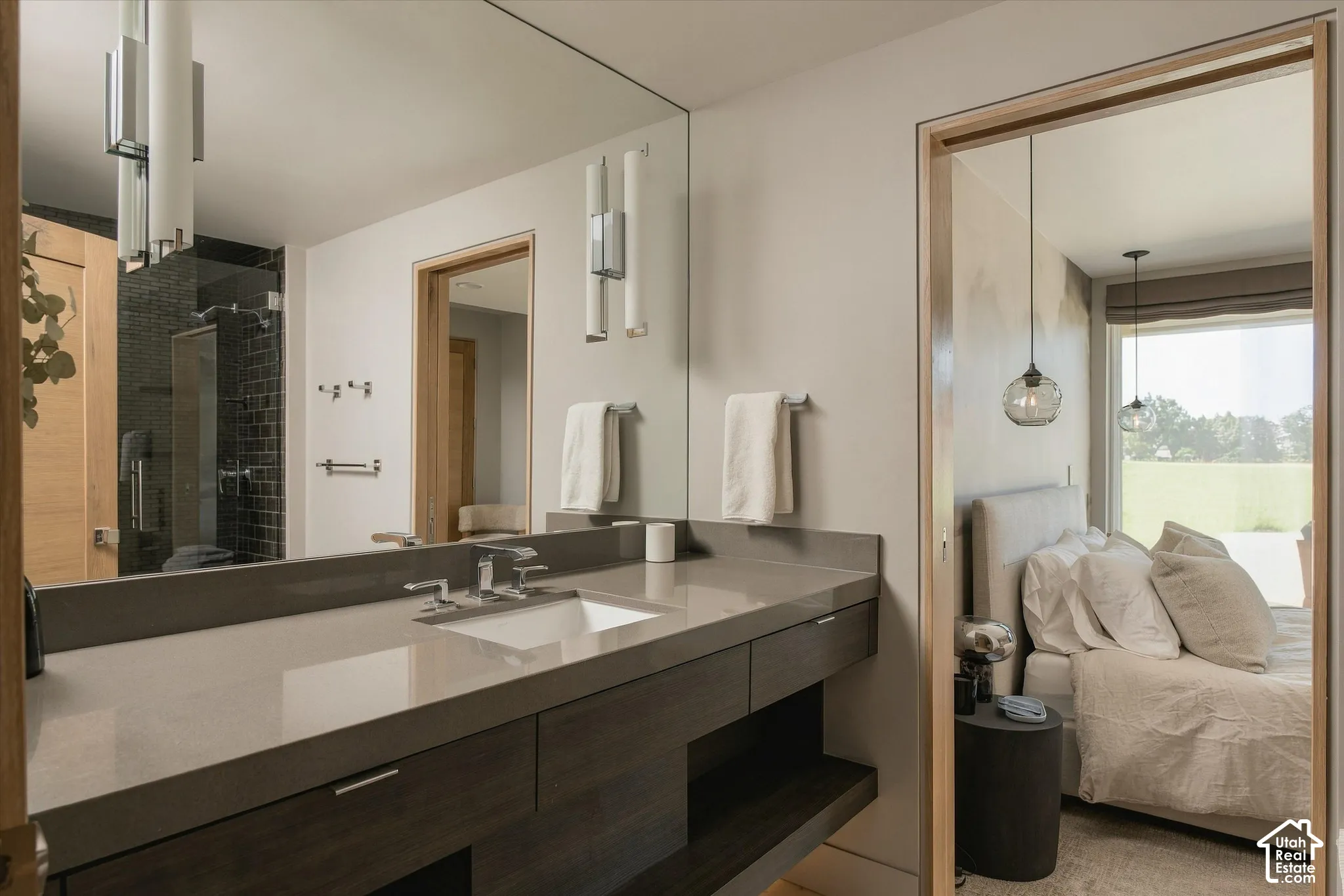 Floating vanity with integrated sink, full-width mirror, wall-mounted sconces, and a glass-enclosed shower