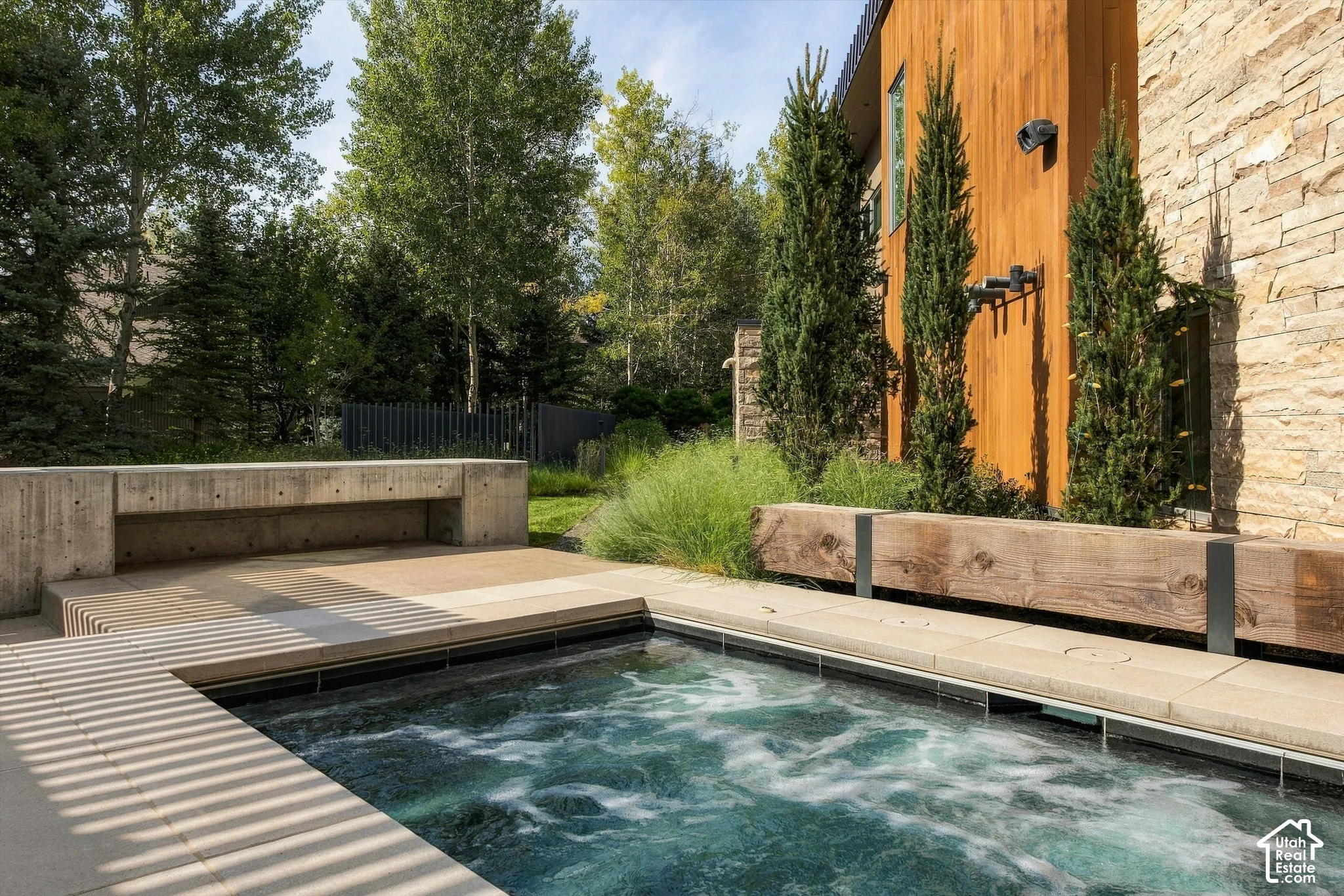 Plunge pool featuring a concrete surround, integrated concrete bench, wood-clad architectural element, and stone facade