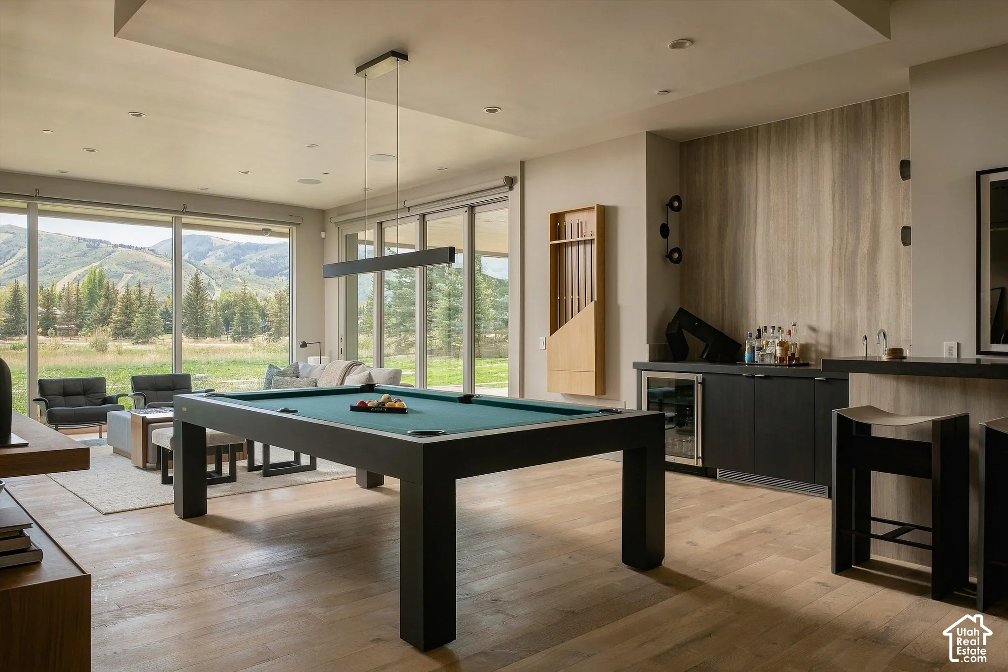 Expansive floor-to-ceiling windows, wood-finish flooring, built-in wet bar with integrated beverage cooler, and recessed lighting