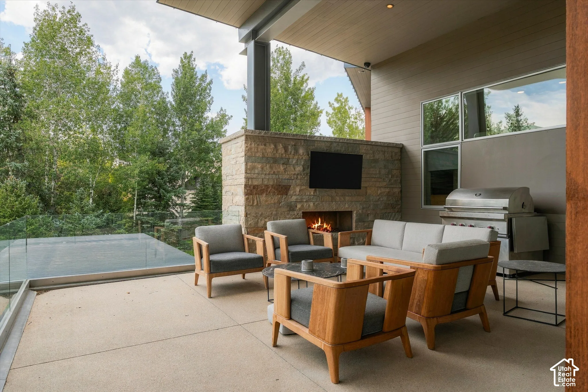 Covered outdoor patio with a stone fireplace, integrated television, built-in grill, and glass railing