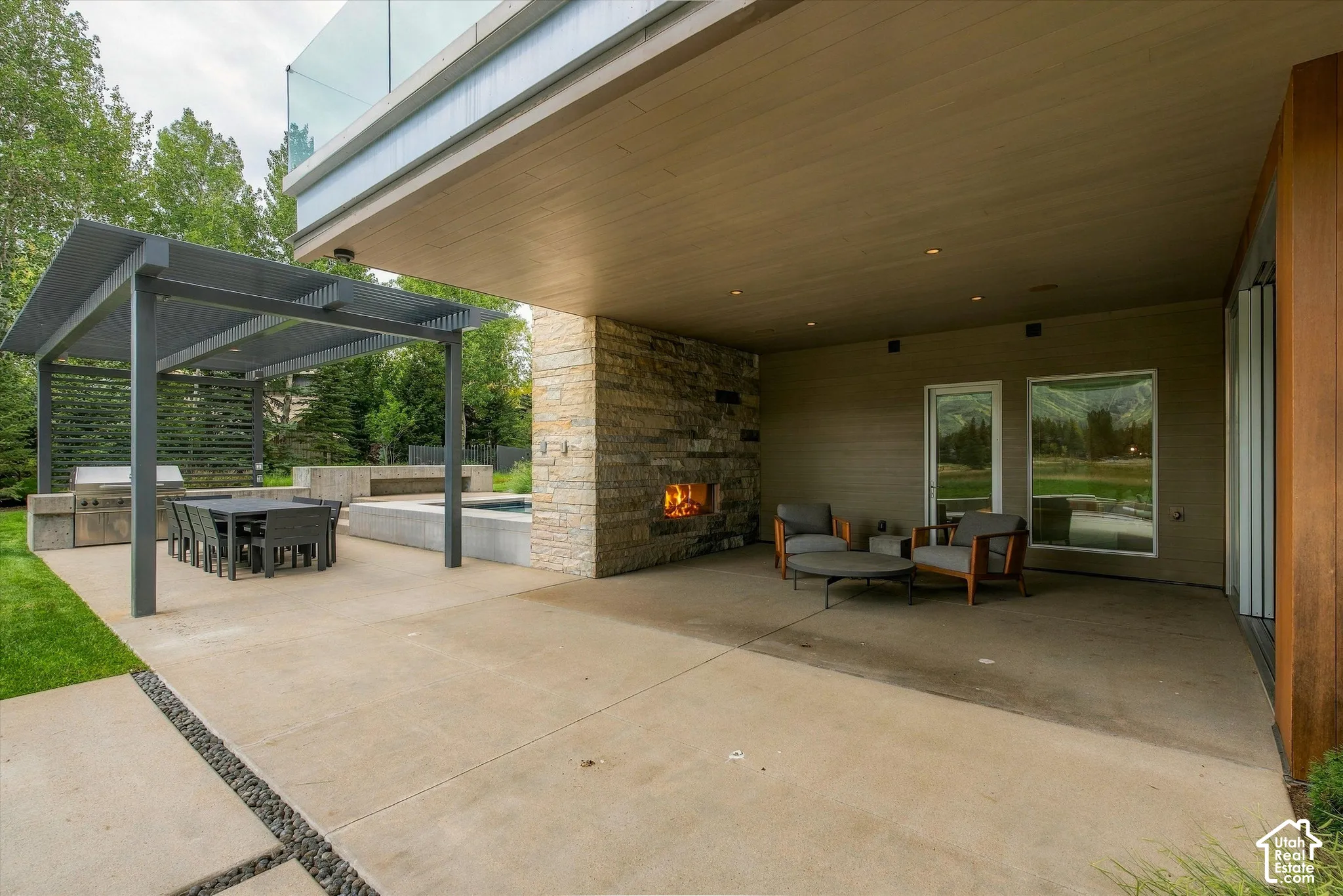 Expansive concrete patio featuring a stone-clad fireplace and recessed lighting
