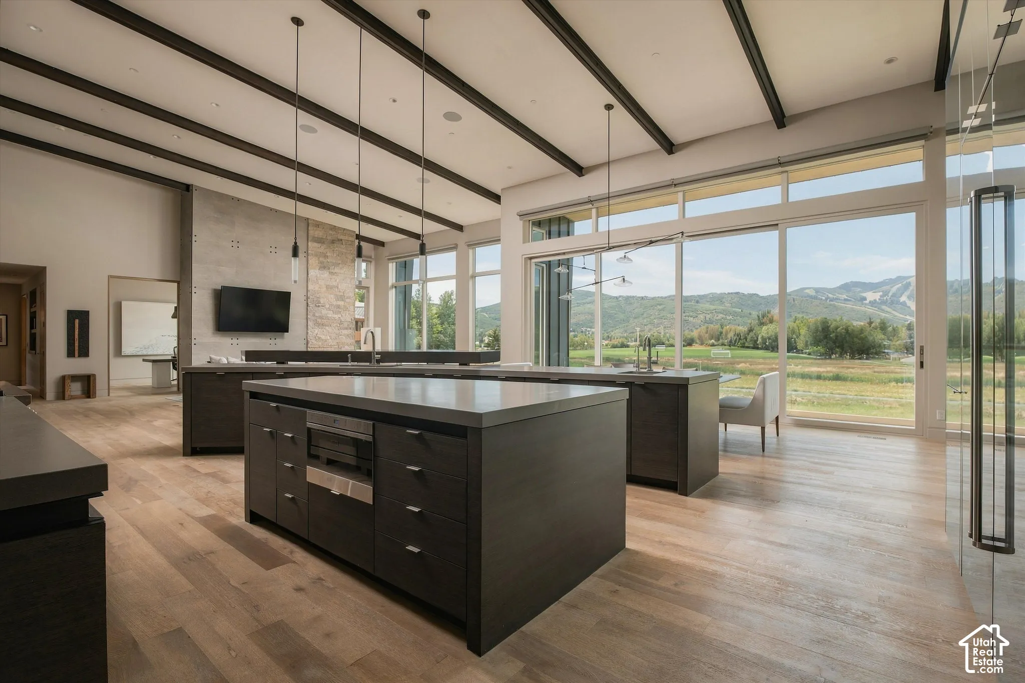 Expansive sliding glass doors, vaulted ceilings with exposed beams, wood-finish flooring, multiple kitchen islands with integrated appliances, and pendant lighting