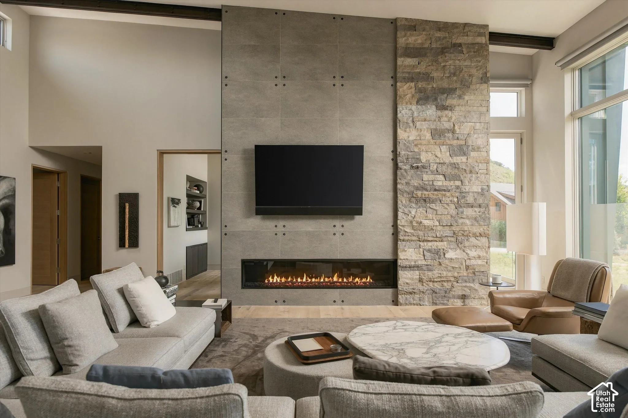 Floor-to-ceiling windows, stone-clad fireplace, integrated linear fireplace, exposed ceiling beams, and high ceilings