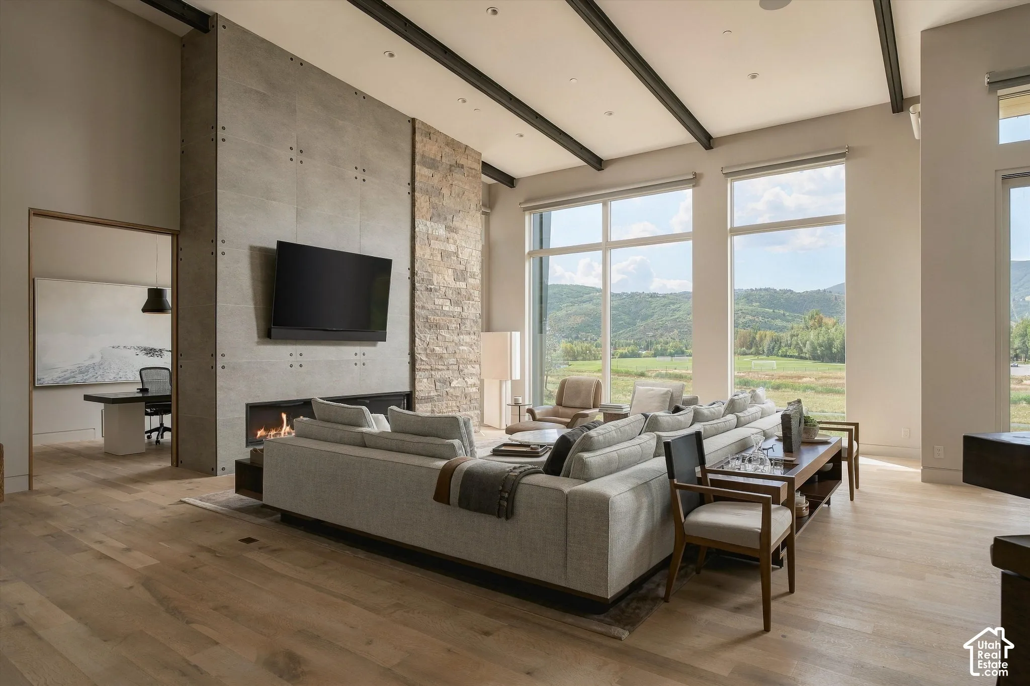Vaulted ceilings with exposed beams, wood-finish flooring, a stone and concrete fireplace, and expansive windows