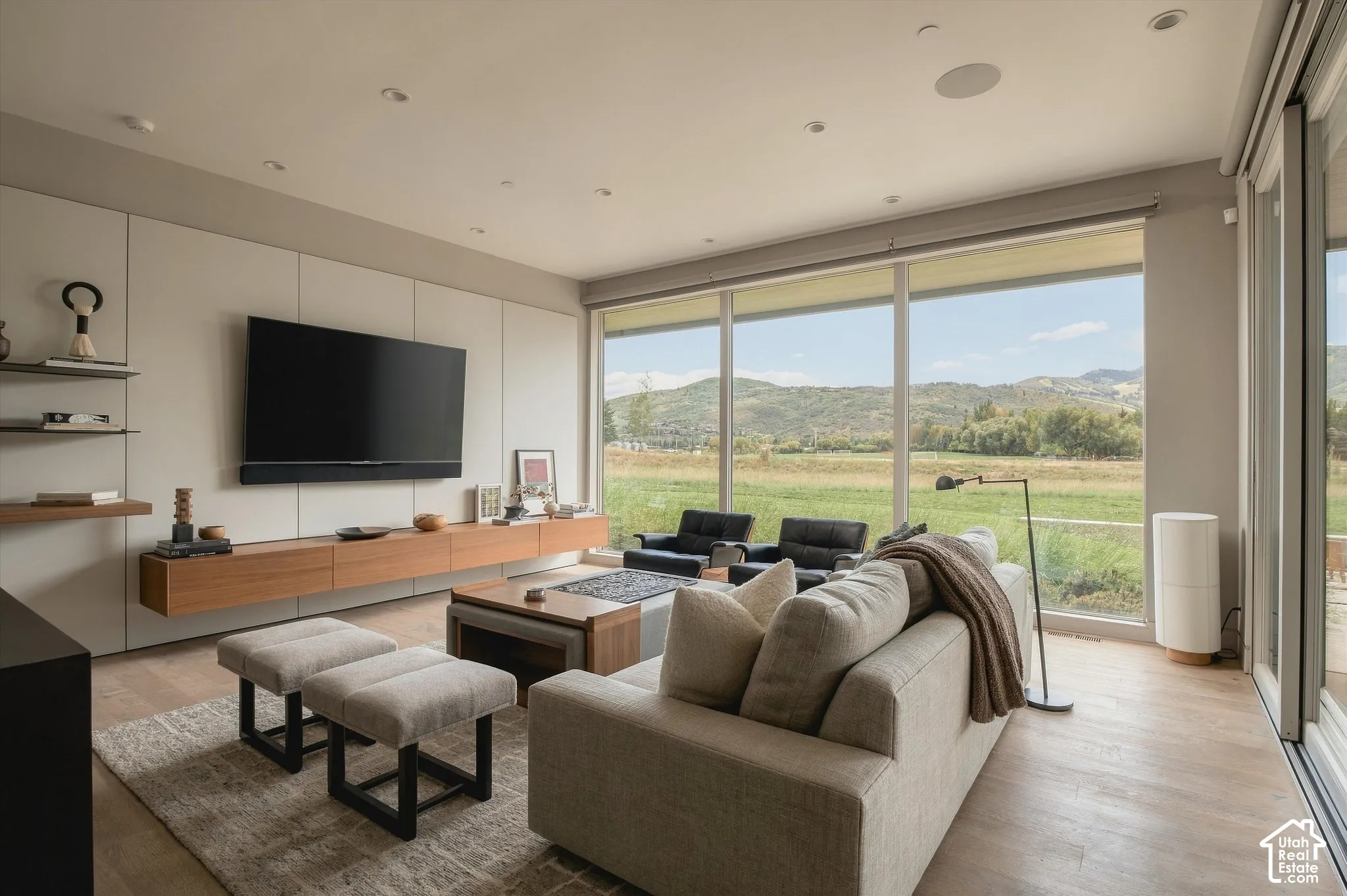 Wall-to-wall glazing with expansive outdoor scenery, wood-finish flooring, built-in wall cabinetry, floating media console, and recessed ceiling lighting