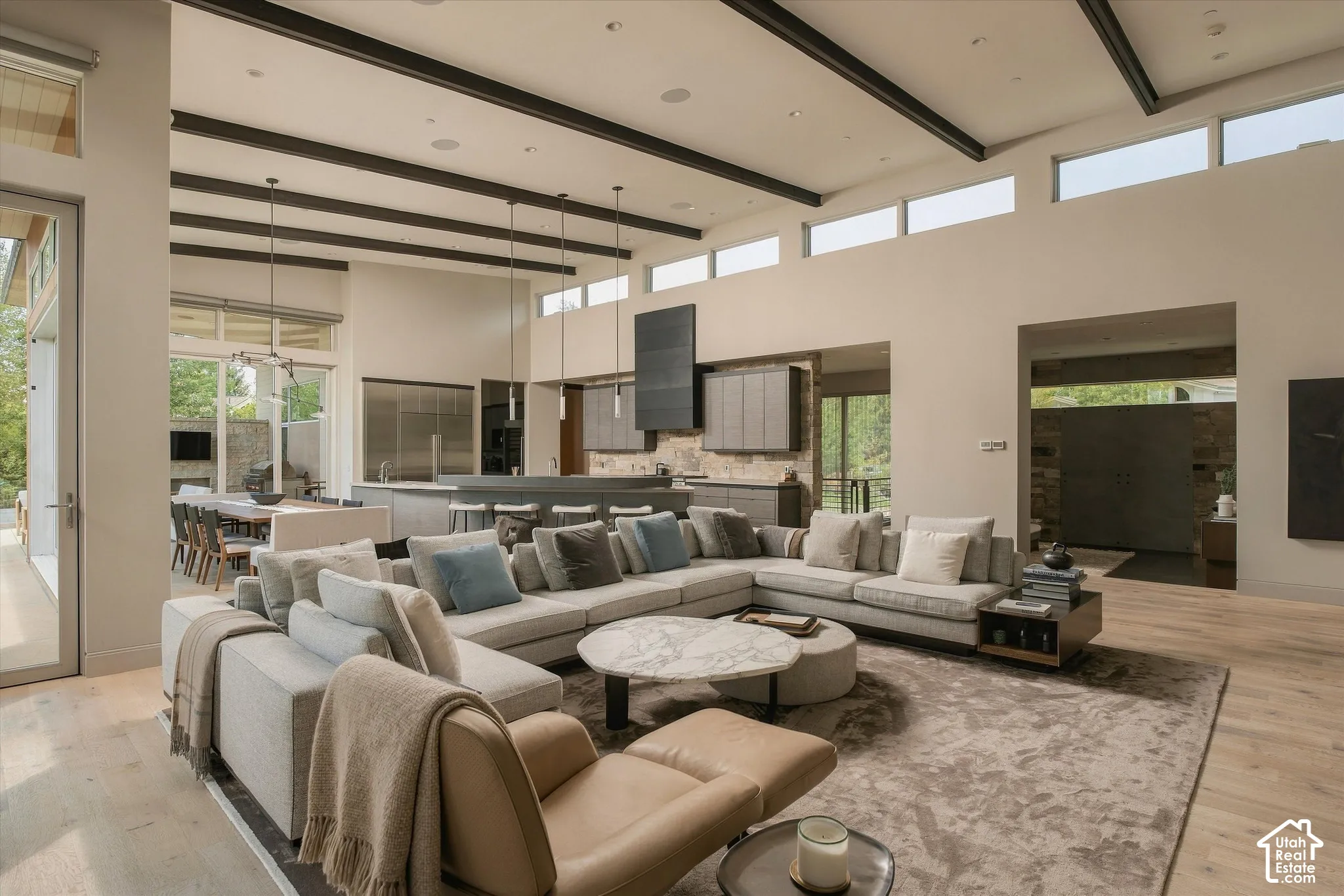 Vaulted ceilings with exposed beams, light wood-finish flooring, recessed lighting, and expansive windows