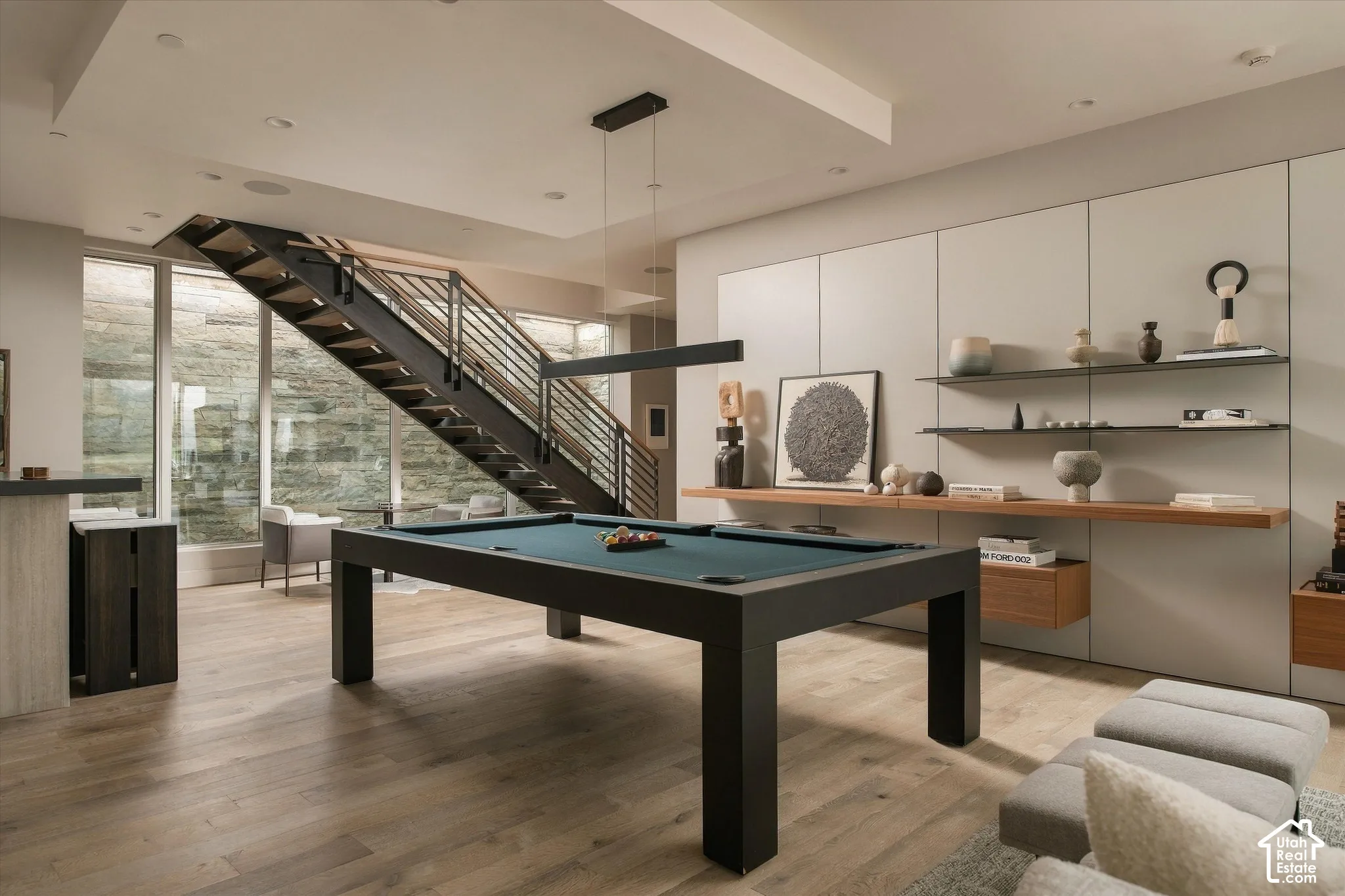 Wood-finish flooring, full-height windows, a metal staircase with horizontal railings, built-in shelving with wood and metal elements, and recessed lighting