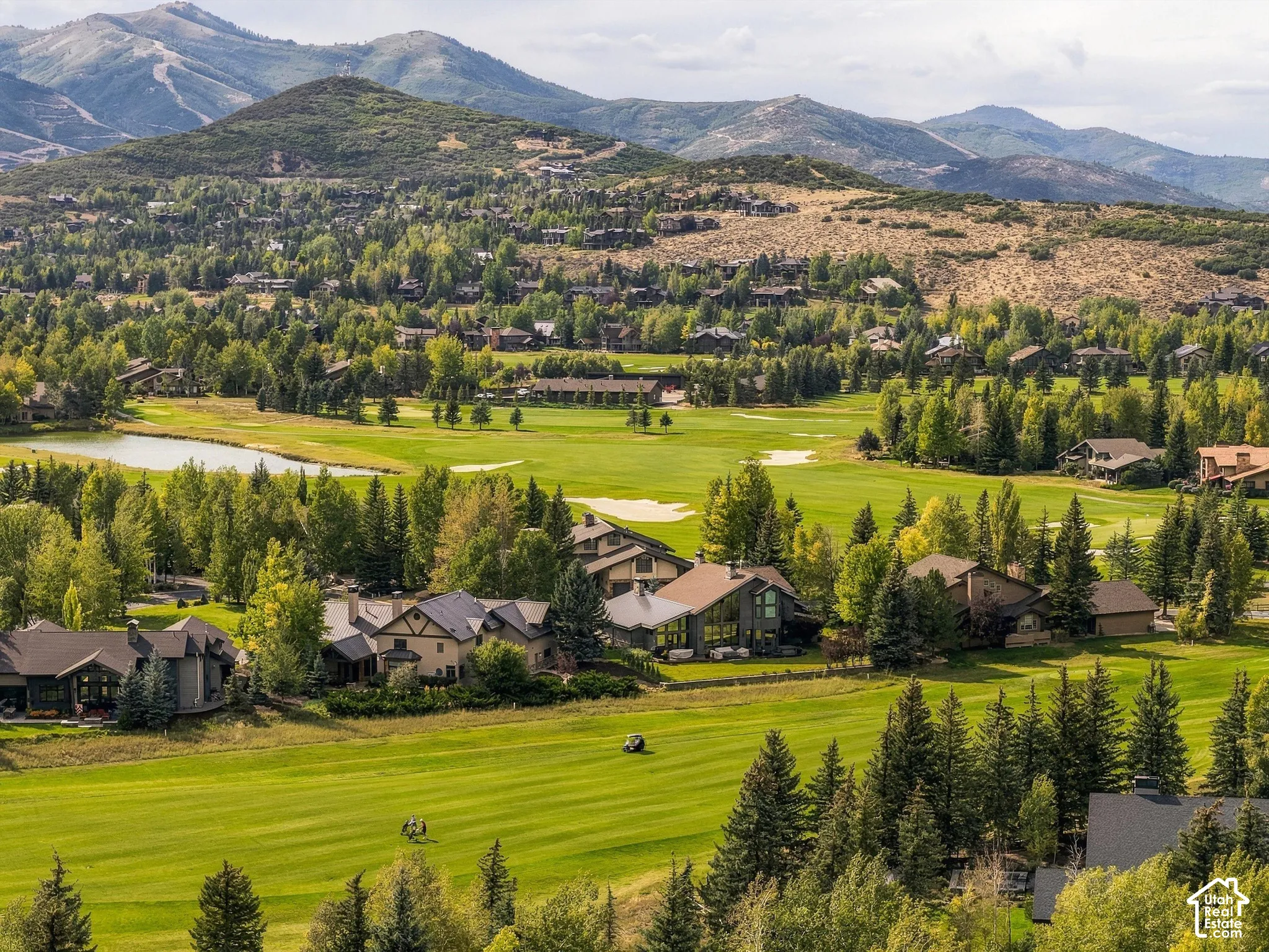 Expansive golf course with surrounding residential properties, mature trees, and mountainous terrain