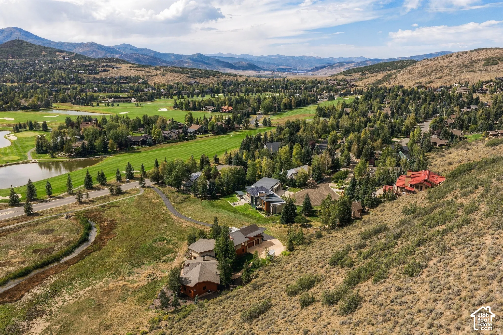 Expansive landscape featuring golf course fairways, multiple water features, mature trees, and mountainous terrain