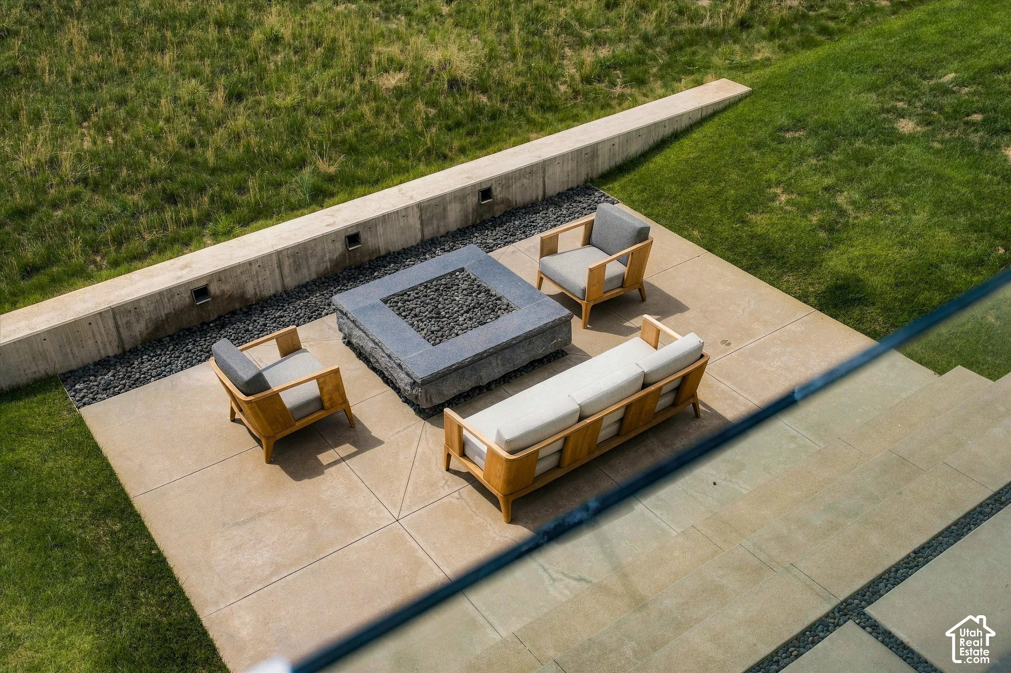 Hardscaped patio with a built-in fire pit, surrounded by a concrete retaining wall with integrated lighting