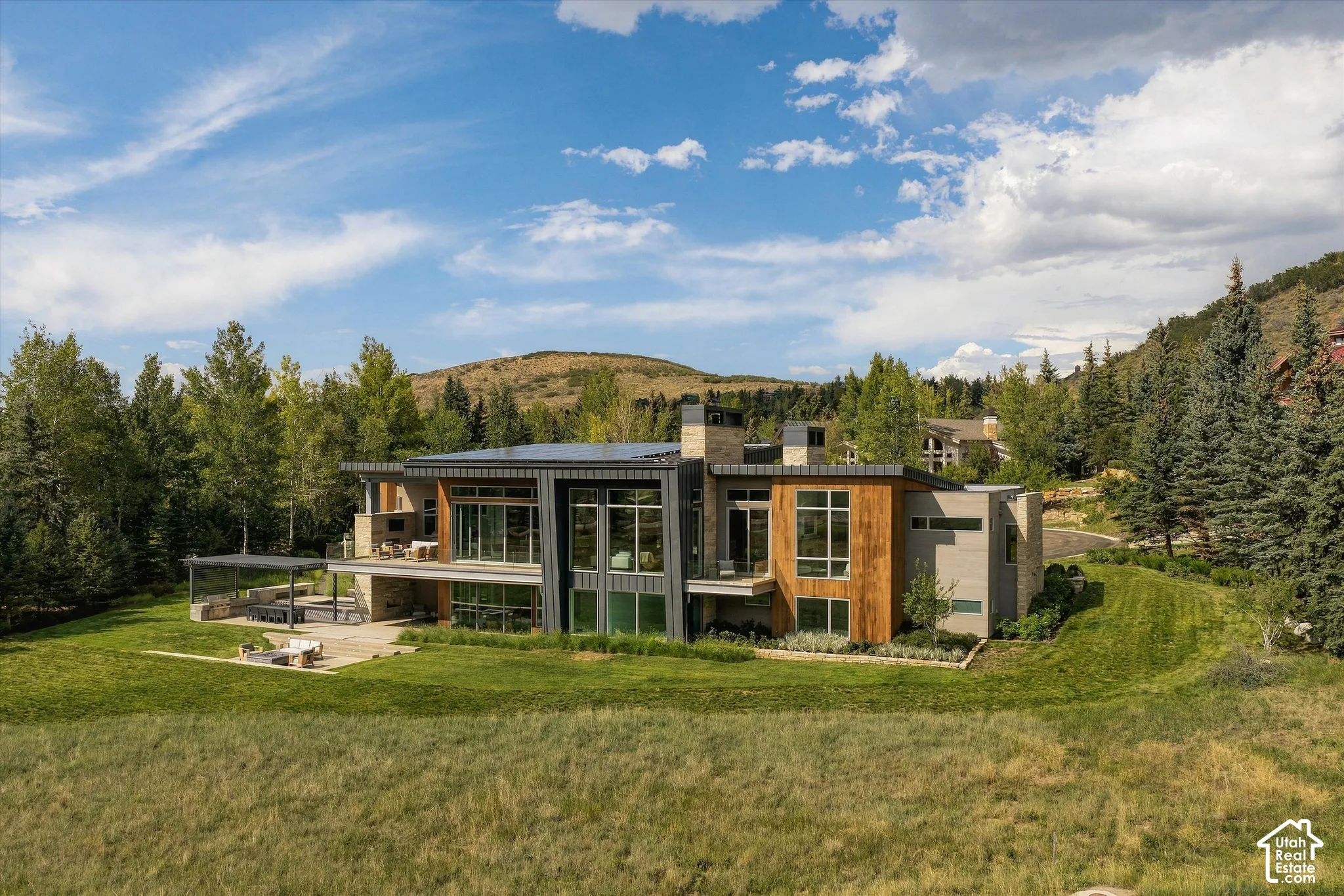 Contemporary architectural style with extensive glazing, wood-panel accents, stone façade elements, a covered patio, and a second-story balcony