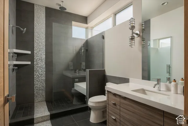 Spacious bathroom featuring a glass-enclosed shower with contrasting tile mosaic, dual shower heads, and built-in shelving