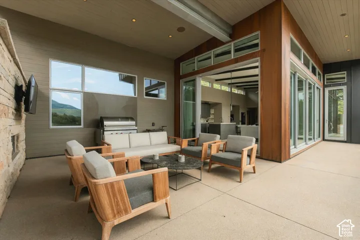 Expansive outdoor patio featuring a stacked stone wall, built-in outdoor grill, a series of multi-panel sliding glass doors, and large fixed-pane windows
