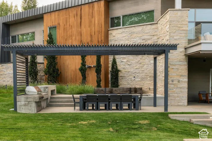 Expansive lawn with a concrete patio featuring a metal pergola, built-in concrete grill station, and outdoor dining area