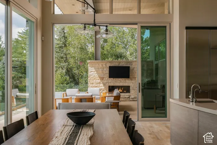 Expansive glass sliding doors, stone fireplace with television, wood-finish flooring, built-in kitchen cabinetry, and a large outdoor patio