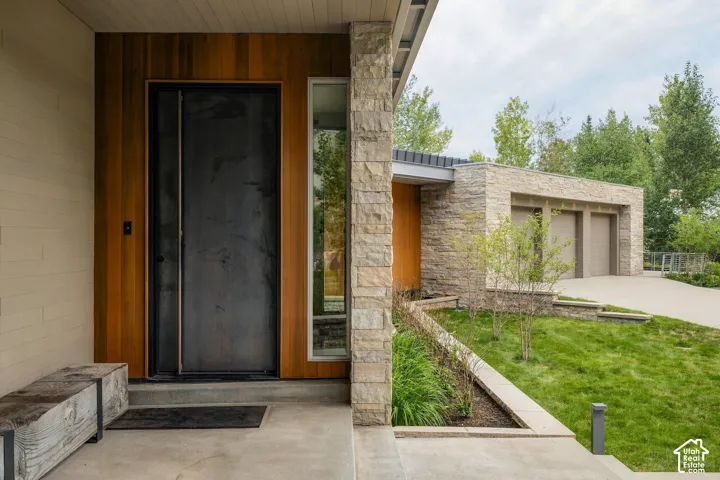 Stone facade, wood-clad entryway, modern dark entry door, concrete driveway, and integrated garage