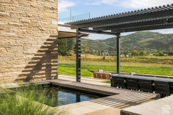 Stacked stone exterior, integrated water feature, wood-finish decking, shaded pergola, glass balcony railing