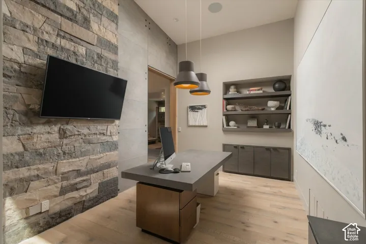 Stacked stone accent wall, recessed shelving, built-in cabinetry, wood-finish flooring, and suspended pendant lighting