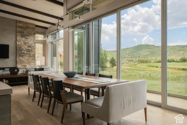 Floor-to-ceiling windows, wood-finish flooring, exposed beam ceiling, stone accent wall, and a linear pendant light fixture