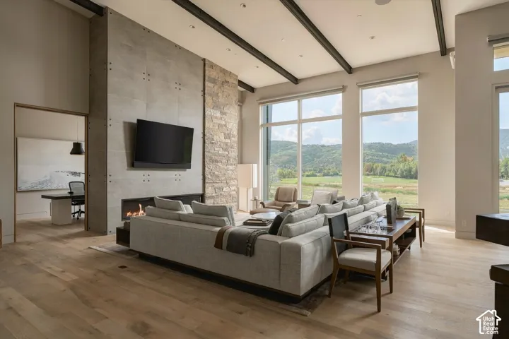 Vaulted ceilings with exposed beams, wood-finish flooring, a stone and concrete fireplace, and expansive windows