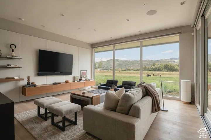 Wall-to-wall glazing with expansive outdoor scenery, wood-finish flooring, built-in wall cabinetry, floating media console, and recessed ceiling lighting