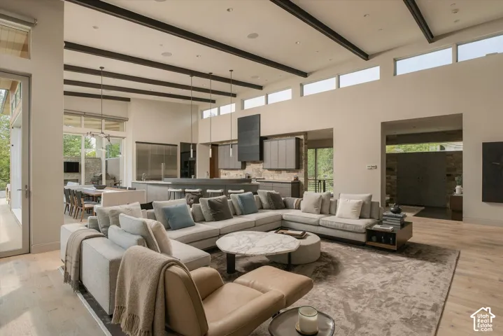 Vaulted ceilings with exposed beams, light wood-finish flooring, recessed lighting, and expansive windows