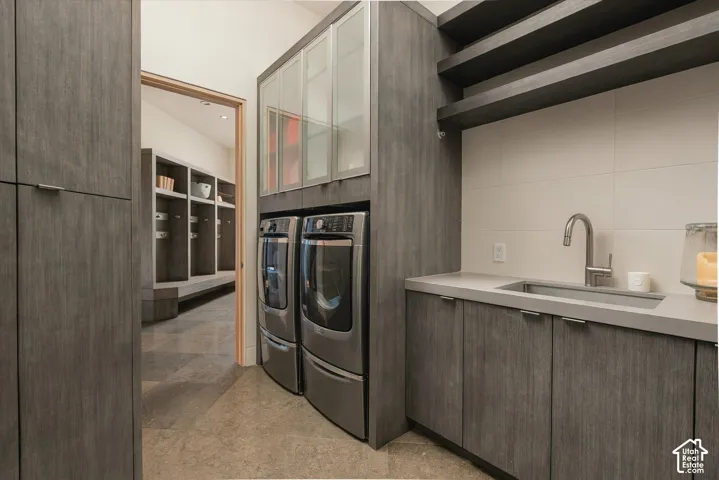 Laundry room featuring textured wood-finish cabinetry, integrated stainless steel sink, light-toned countertop, and white tile backsplash