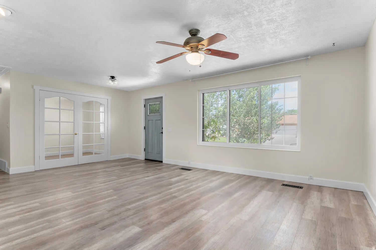 Bright living area featuring wood-finish flooring, a large multi-pane window, and a ceiling fan with integrated lighting