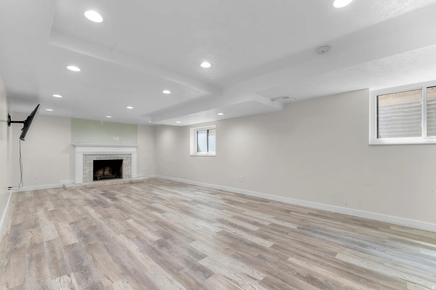 Spacious room in Basement featuring wood-finish flooring, a white mantel fireplace with a tiled surround, recessed lighting, and a window providing natural light