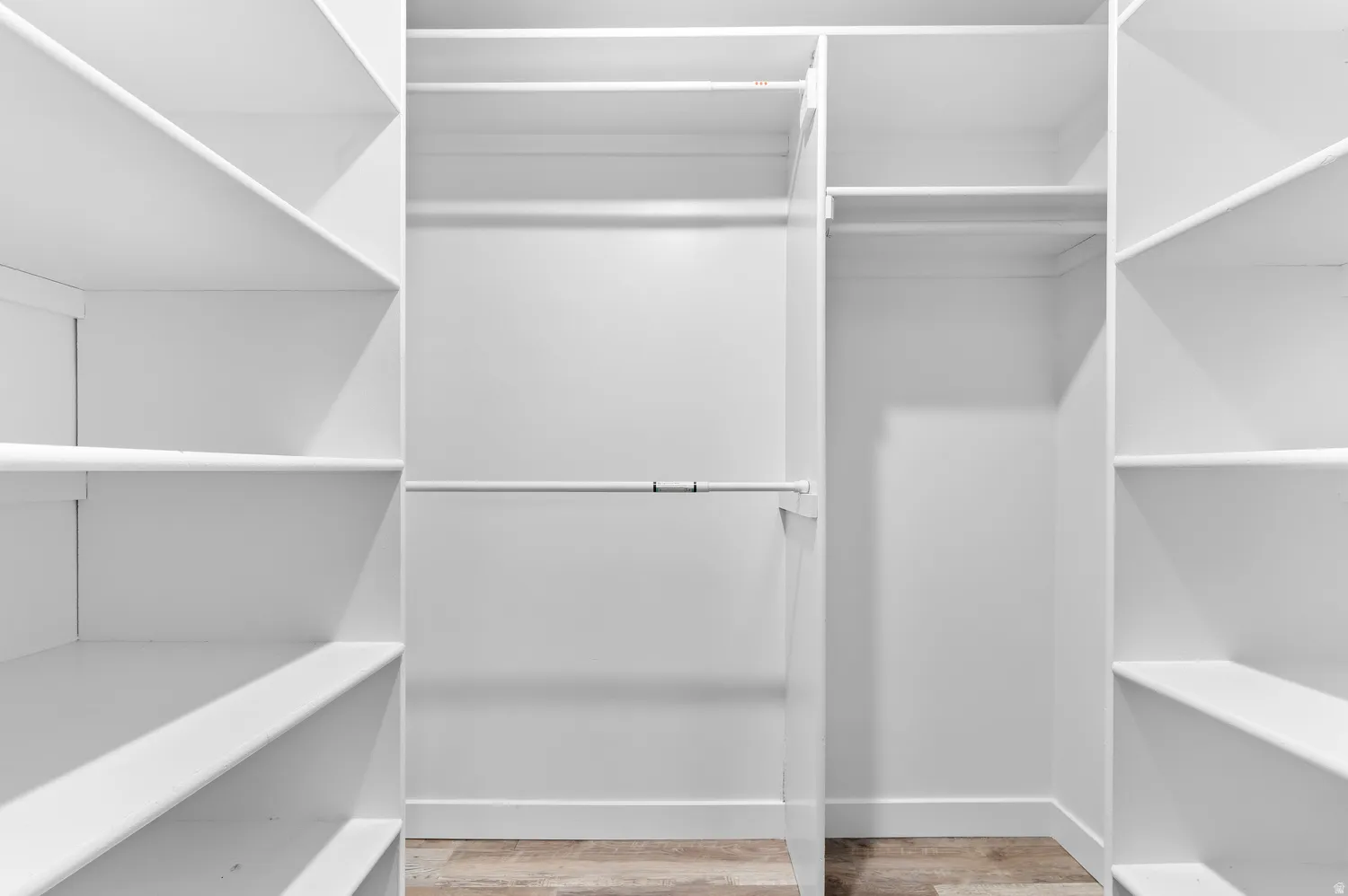Walk-in Master closet featuring white built-in shelving, multiple hanging rods, and wood-finish flooring