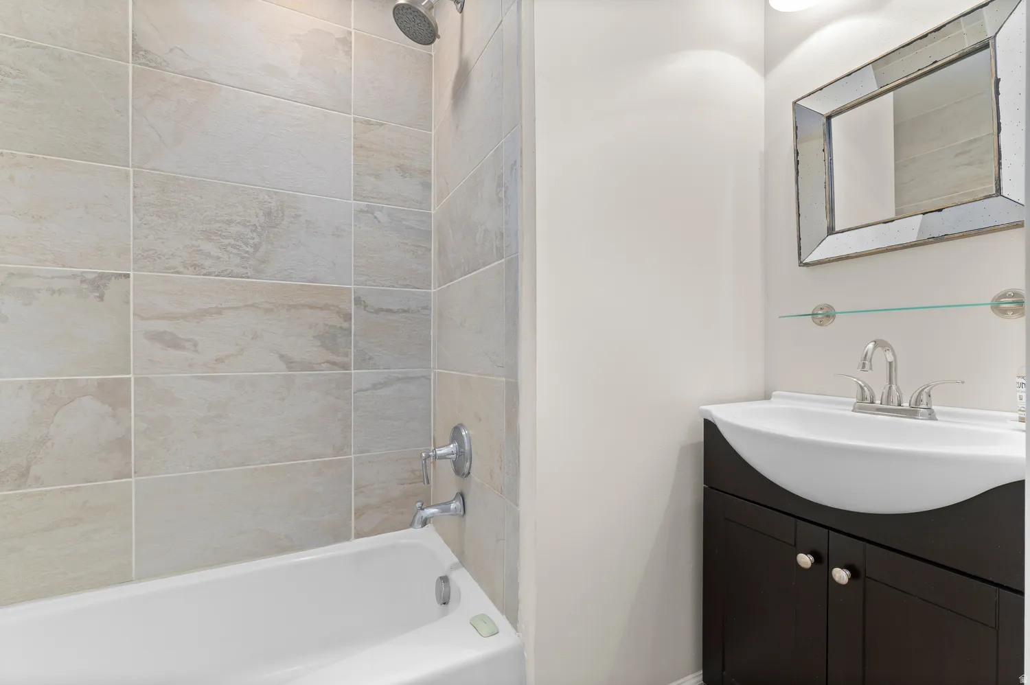 2nd main Bathroom featuring a white tub, light-toned rectangular tile surround, dark wood-finish vanity with an integrated white sink, and a framed mirror