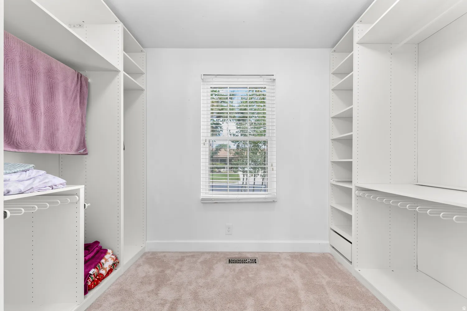 Walk-in Master closet featuring white built-in shelving, white walls, and a window with white blinds