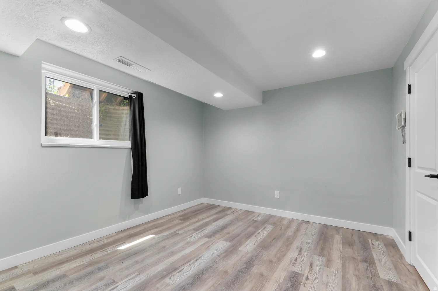 Room featuring light wood-finish flooring, recessed lighting, and a white interior door with black hardware