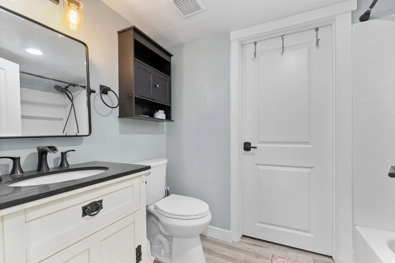 Bathroom featuring a white vanity with black countertop, matte black fixtures, rectangular mirror, and white subway tile shower surround
