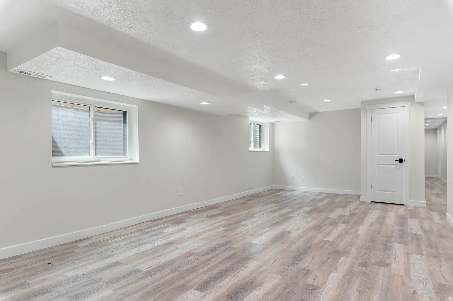 Spacious room featuring light wood-finish flooring, white walls, and recessed lighting