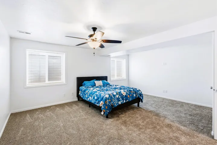 Bedroom #4 New carpeted room featuring a ceiling fan with light fixture, two windows with blinds, and freshly painted white walls.