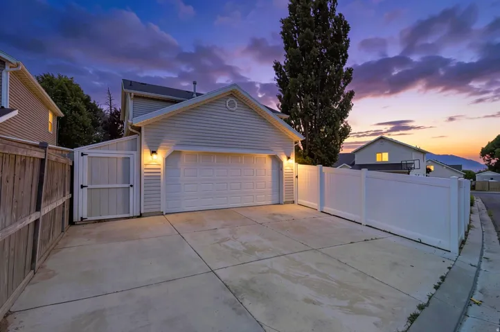Concrete driveway leading to a two-car garage with a white panel door, and custom built oversized shed