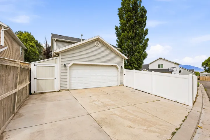 Exterior featuring light-colored siding, an attached garage with a white sectional door, a concrete driveway, oversized custom shed attached and a white privacy fence