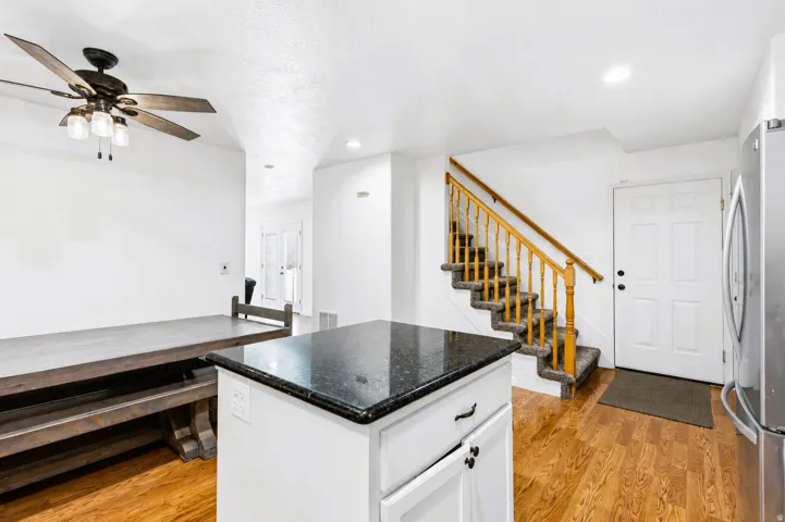 Open-concept living space featuring wood-finish flooring, a white kitchen island with a granite countertop, and a carpeted staircase with wood banisters