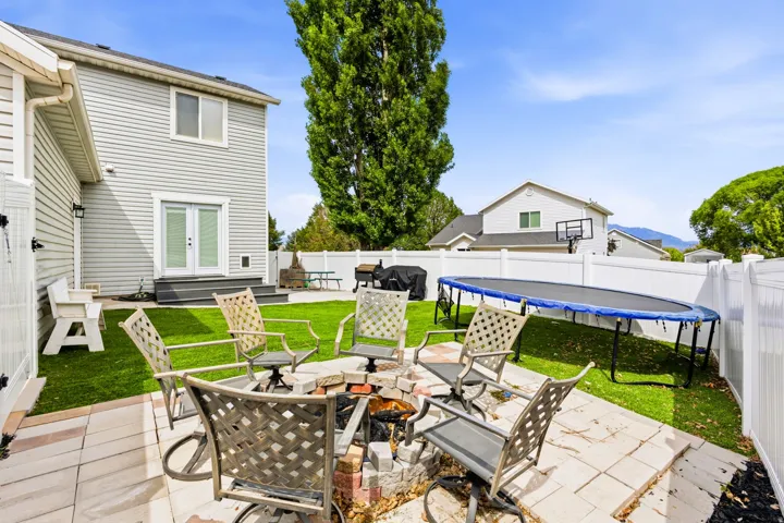 Backyard entertainment area featuring a paver patio with fire pit, artificial turf, and white vinyl fencing