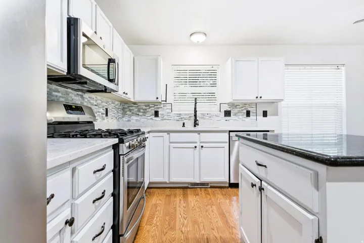 Kitchen featuring white shaker cabinetry, stainless steel appliances, a tile backsplash, quartz countertops and a central island with a granite countertop