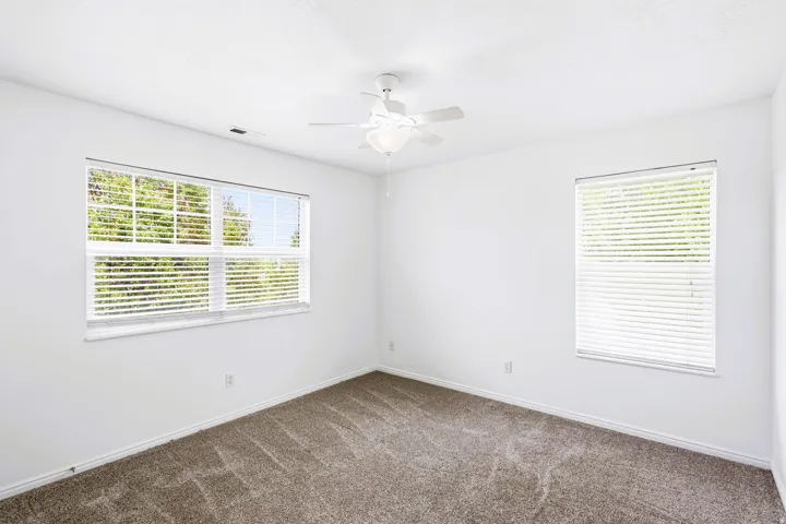 Bedroom #3 Bright interior space featuring two windows with white blinds, neutral carpeting, white baseboards, and a ceiling fan with integrated lighting