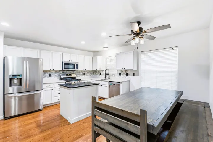 Bright kitchen featuring white cabinetry, stainless steel appliances, a center island with a granite countertop, and laminate flooring.