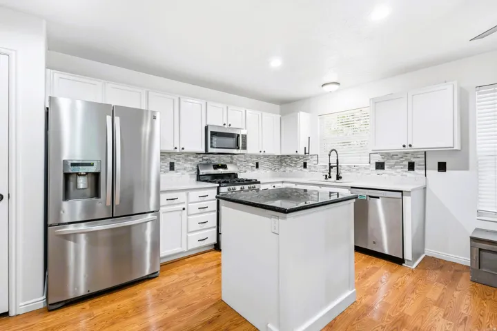Modern kitchen featuring white cabinetry, stainless steel appliances, a center island with granite countertop, light-colored countertops, and wood-finish flooring